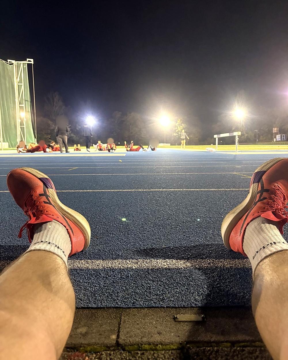 Les chaussures d'un coureur au bord d'une piste d'athlétisme éclairée, la nuit.